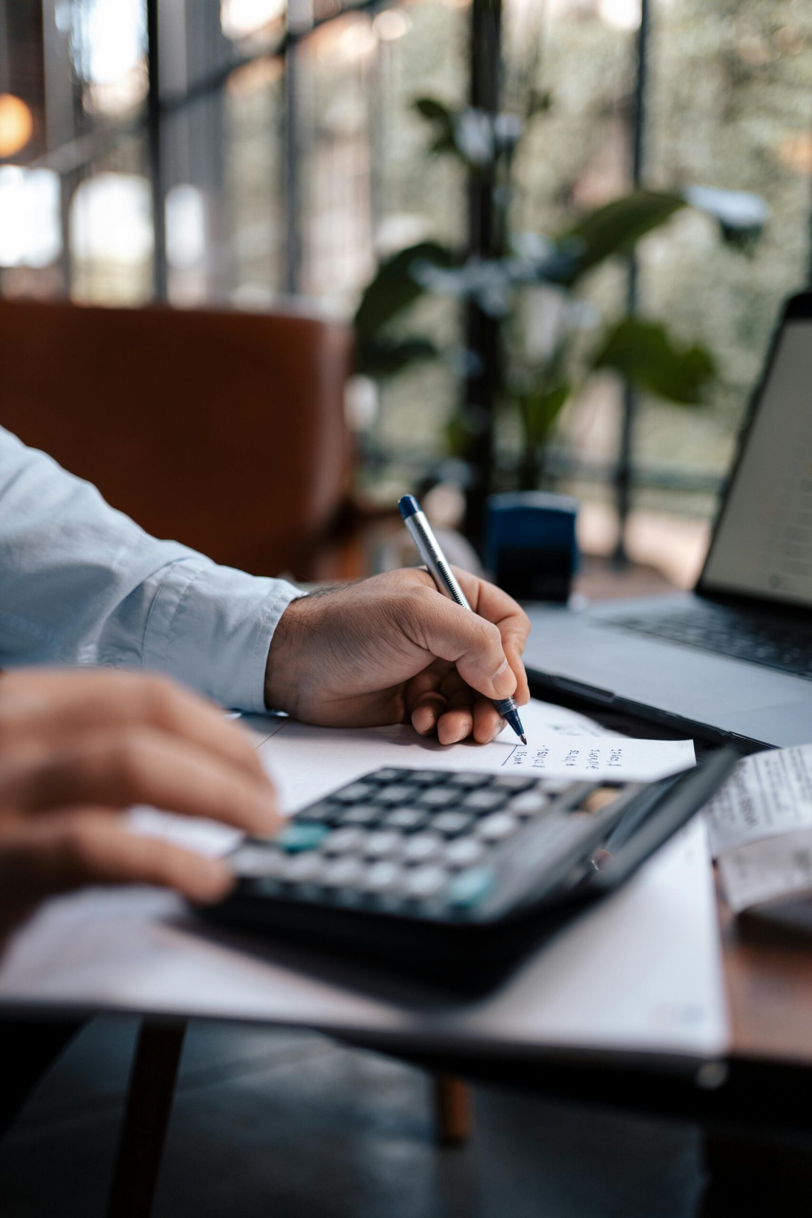 Society accounting management A person calculating finances with a calculator and pen on a desk indoors.
