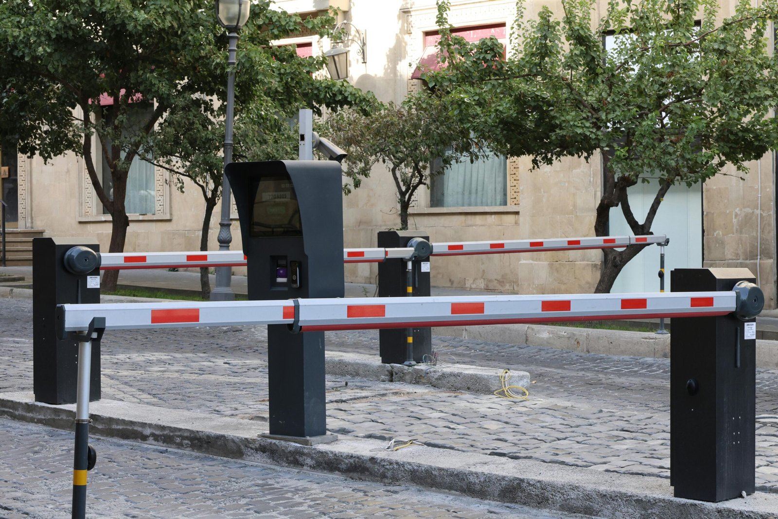 Society Access Control Integration Modern parking barrier gate system on cobblestone street with greenery.
