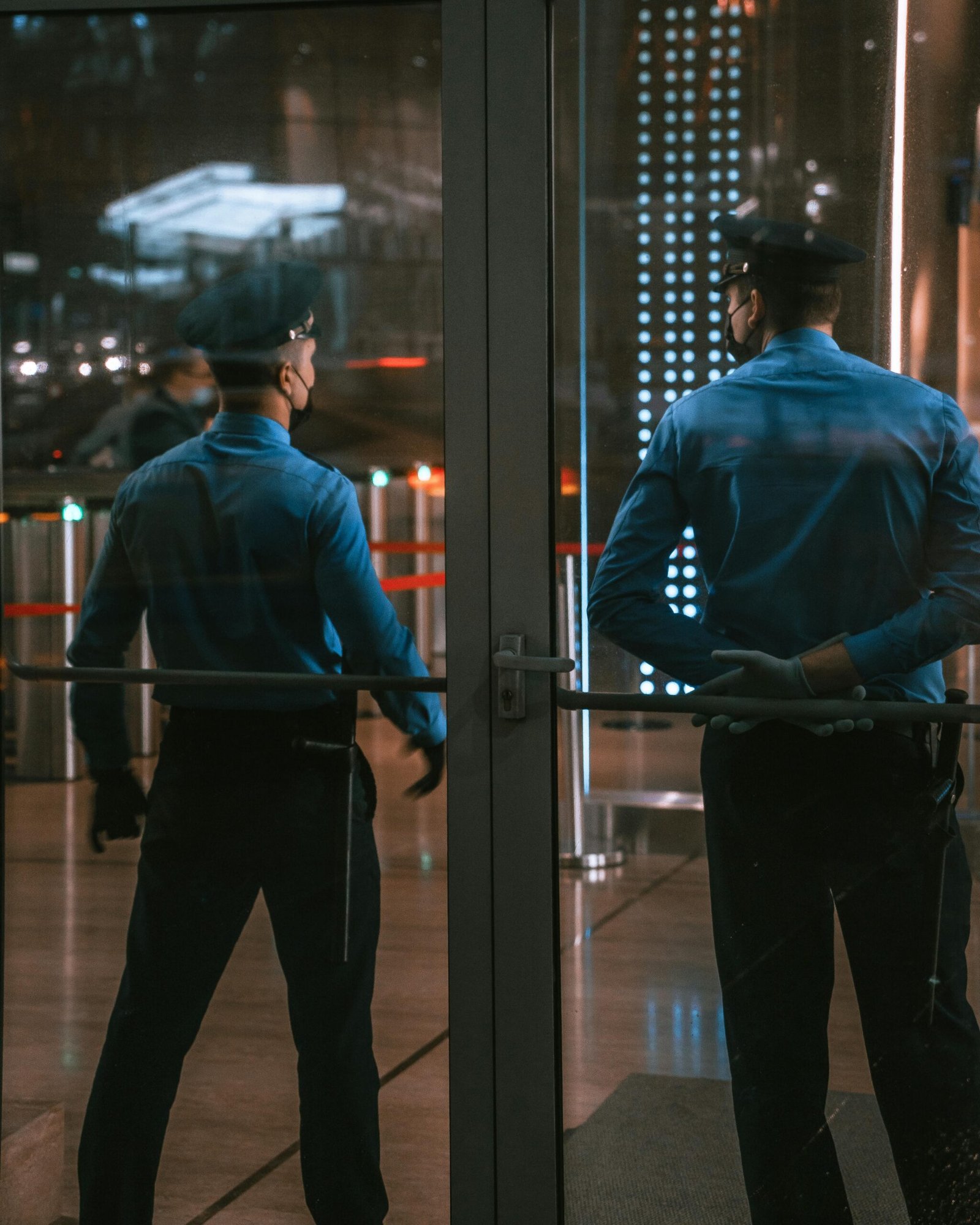 society-visitor-management-system Security guards standing by glass doors, protecting a building entrance at night.