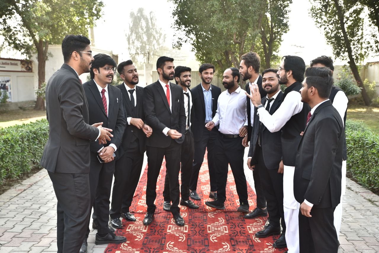 A group of men in formal attire conversing outdoors on a sunny day.