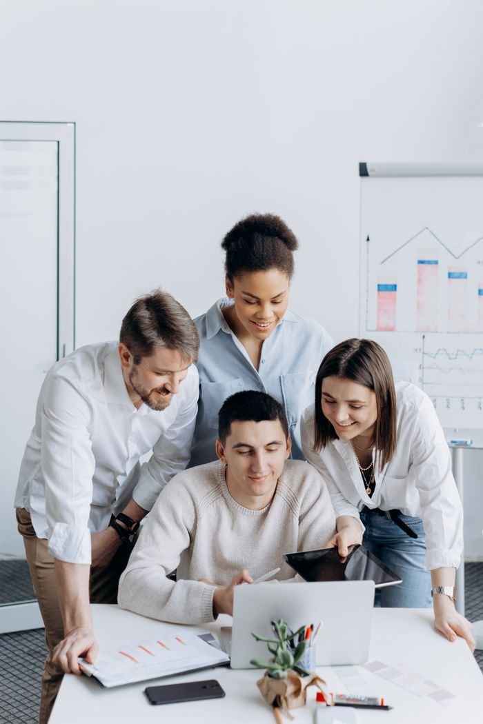 A diverse group of coworkers collaborating on a project with a laptop in an office setting.